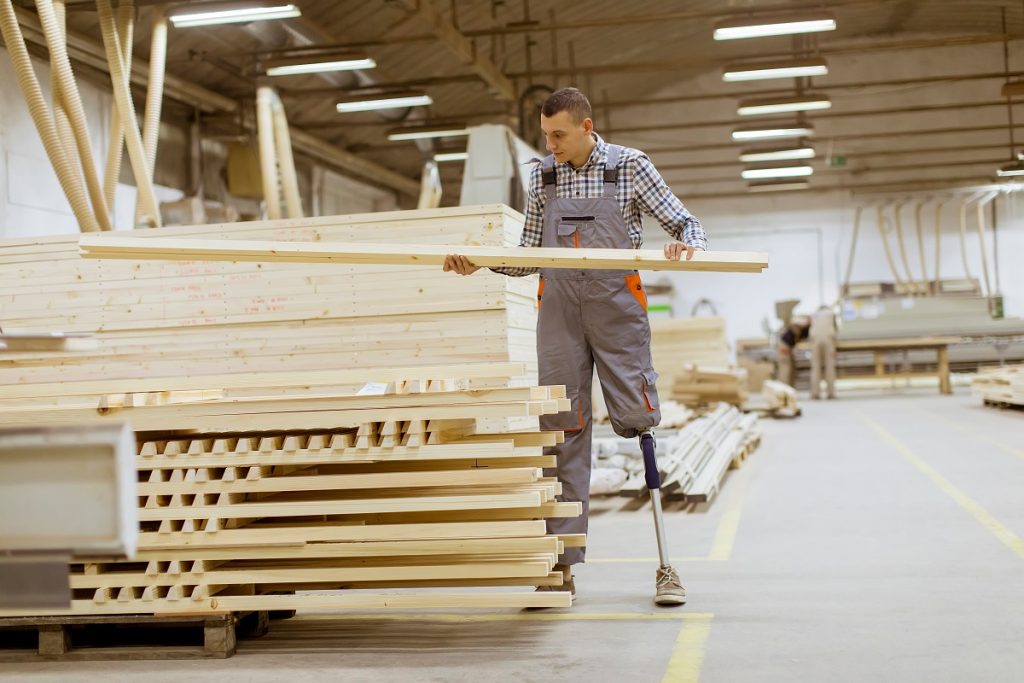  Disabled young man with an artificial leg is working at the furniture factory